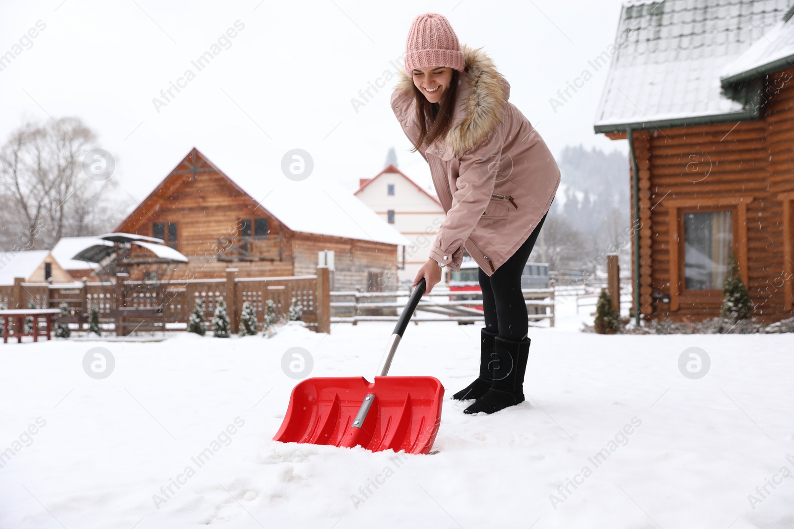 Photo of Young woman cleaning snow with shovel near her house