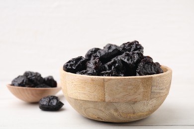 Photo of Bowl and spoon with sweet dried prunes on white table, closeup