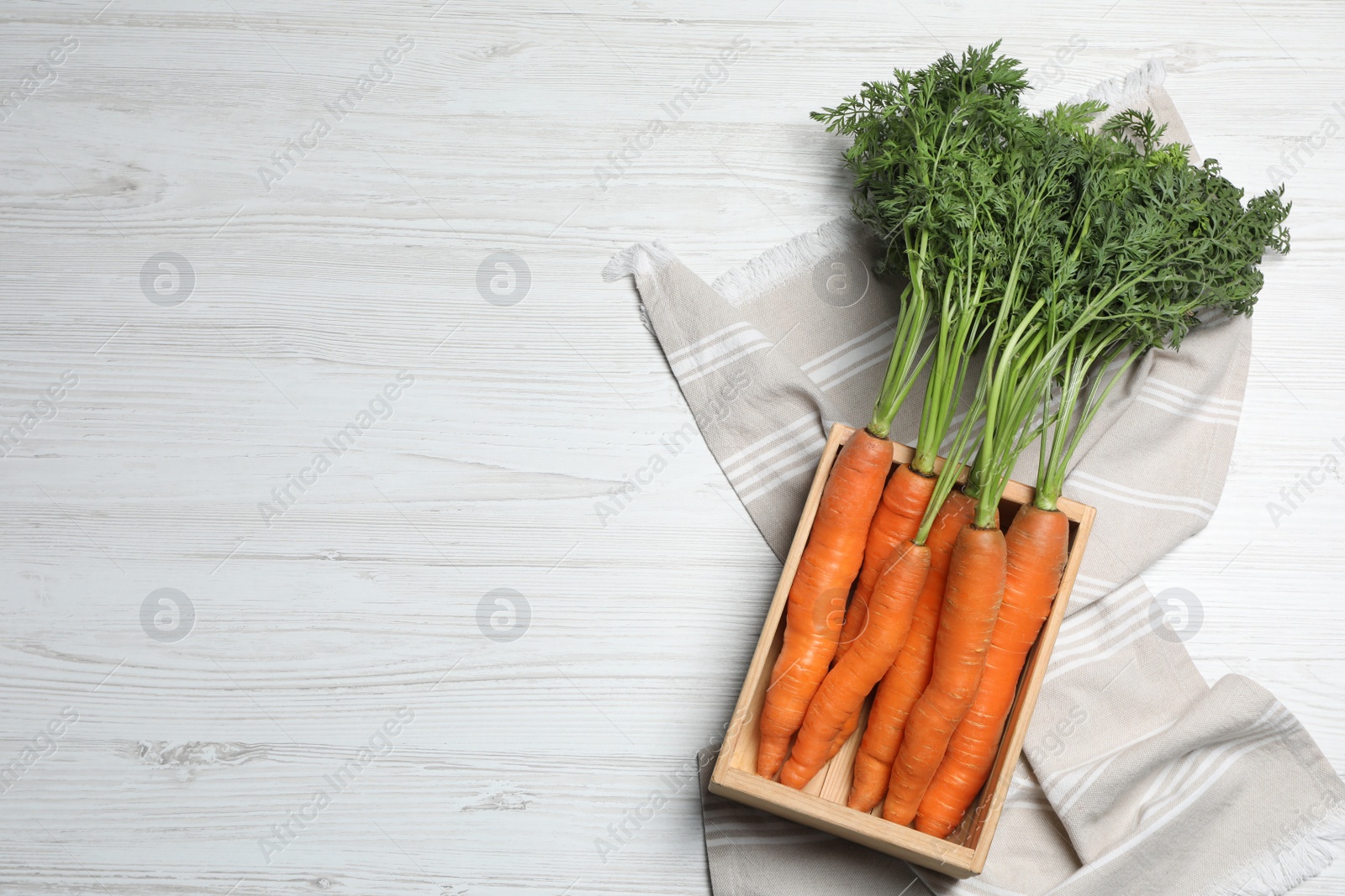 Photo of Fresh carrots in crate on white wooden table, top view. Space for text