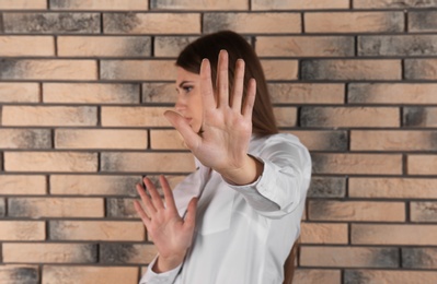 Photo of Woman showing stop gesture near brick wall. Problem of sexual harassment at work