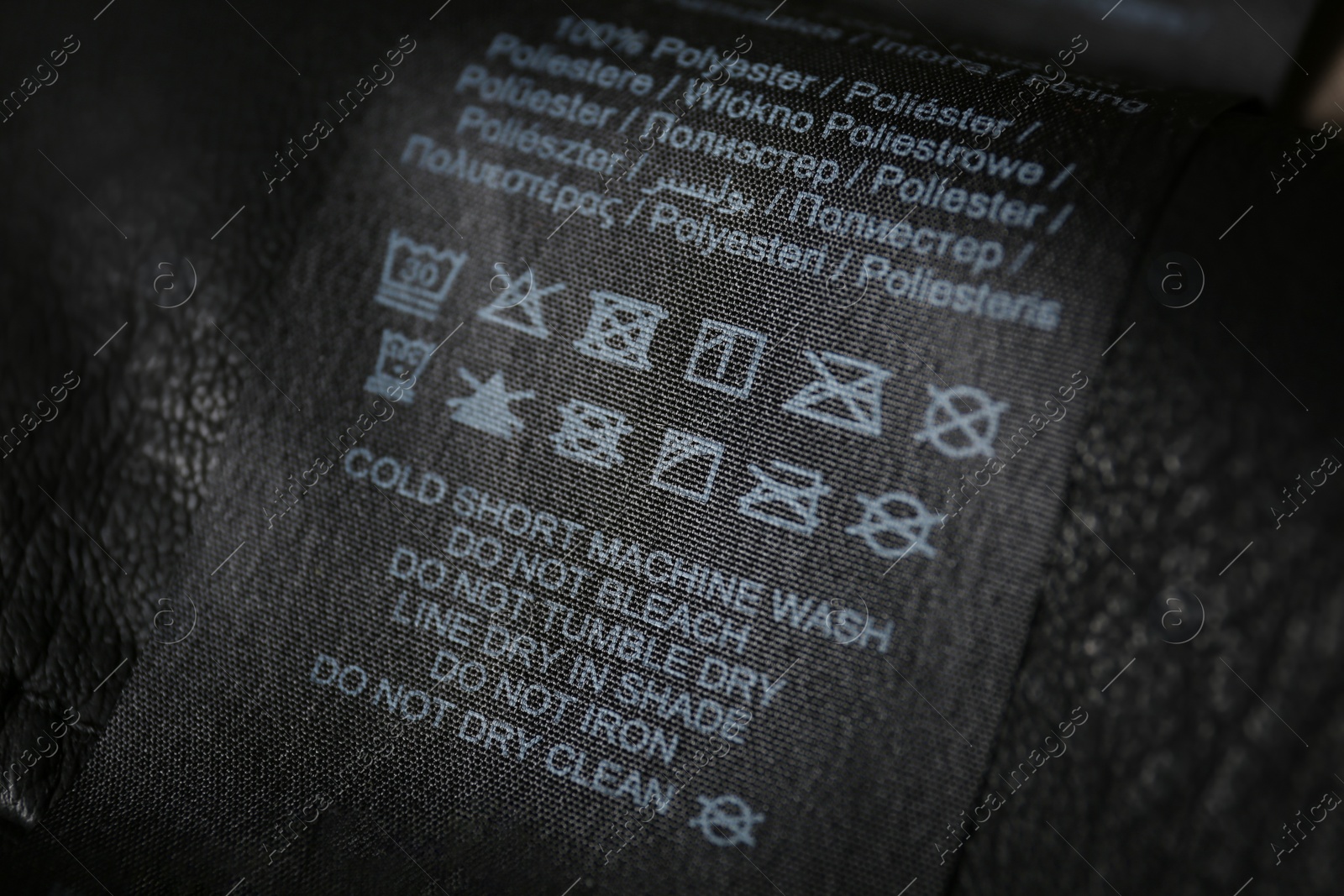 Photo of Clothing label with care symbols and material content on black shirt, closeup view