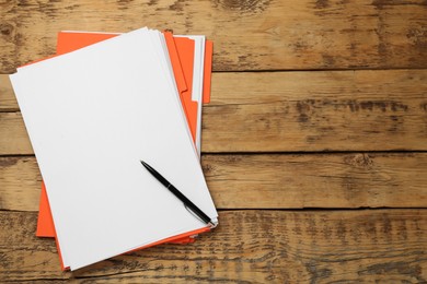 Orange files with blank sheets of paper and pen on wooden table, top view. Space for text