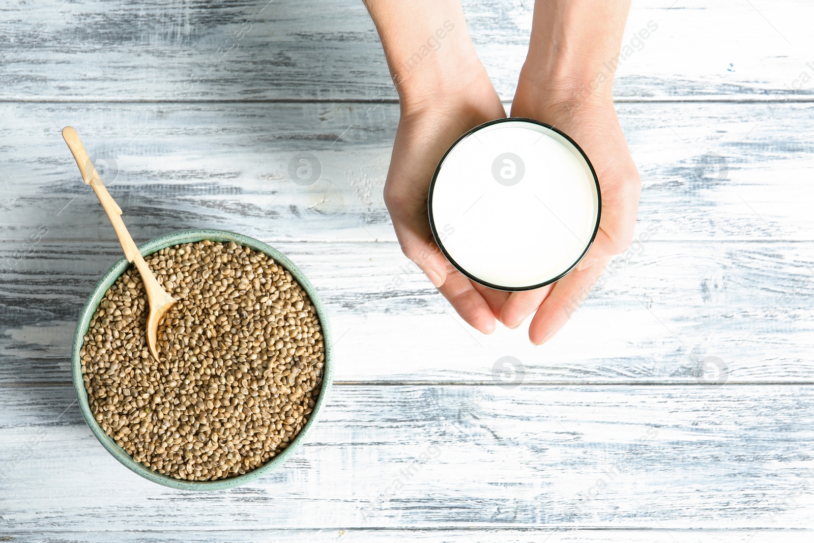 Photo of Woman holding glass of hemp milk over wooden table, top view