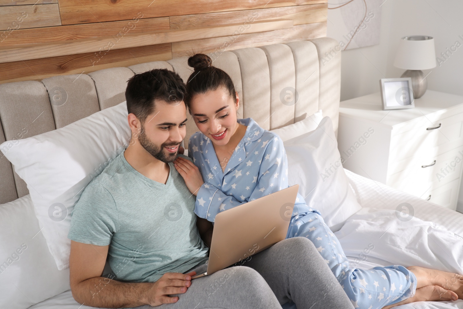 Photo of Happy couple in pajamas with laptop on bed at home