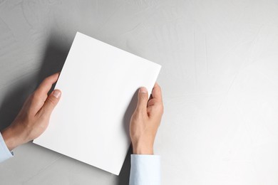 Photo of Man holding blank notebook at light grey table, top view. Mockup for design
