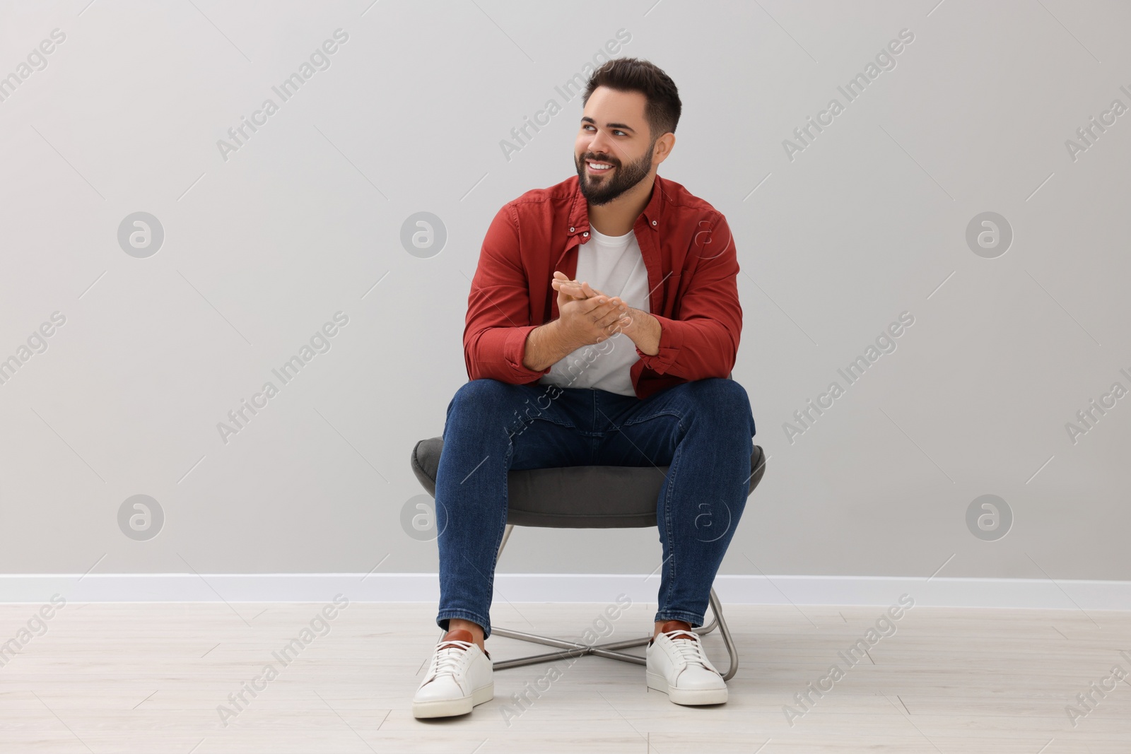 Photo of Handsome man sitting in armchair near light grey wall indoors