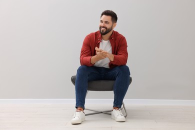 Photo of Handsome man sitting in armchair near light grey wall indoors