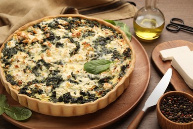 Delicious homemade spinach quiche, spices and knife on wooden table