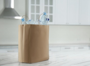 Photo of Paper bag with used plastic bottles on table in kitchen, space for text. Recycling problem