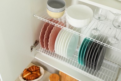 Clean plates, bowls and glasses on shelves in cabinet indoors