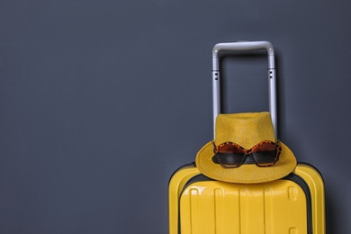 Photo of Bright yellow suitcase with hat and sunglasses on color background