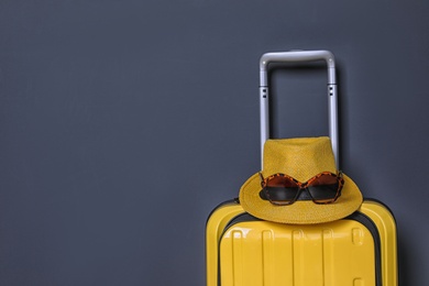 Bright yellow suitcase with hat and sunglasses on color background