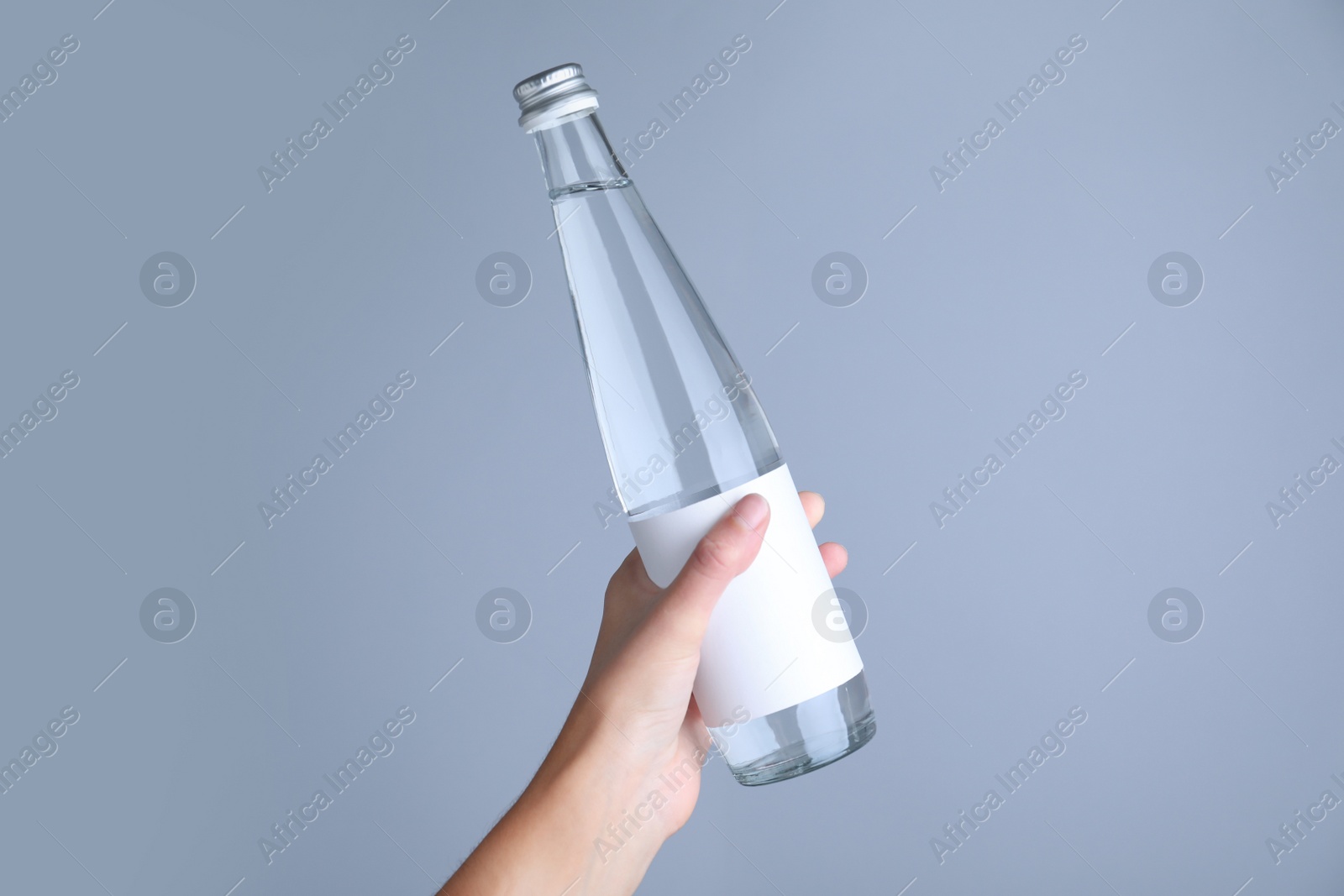 Photo of Woman holding glass bottle with soda water on light grey background, closeup