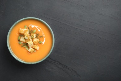 Photo of Delicious pumpkin soup in bowl on black table, top view. Space for text
