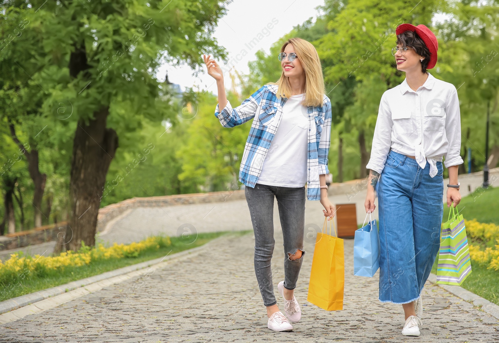 Photo of Young women with shopping bags walking in park