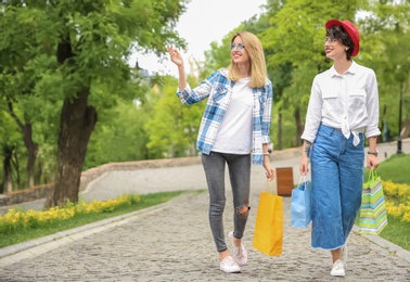 Photo of Young women with shopping bags walking in park