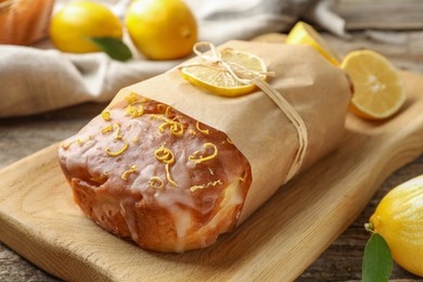 Photo of Wrapped tasty lemon cake with glaze on wooden board, closeup