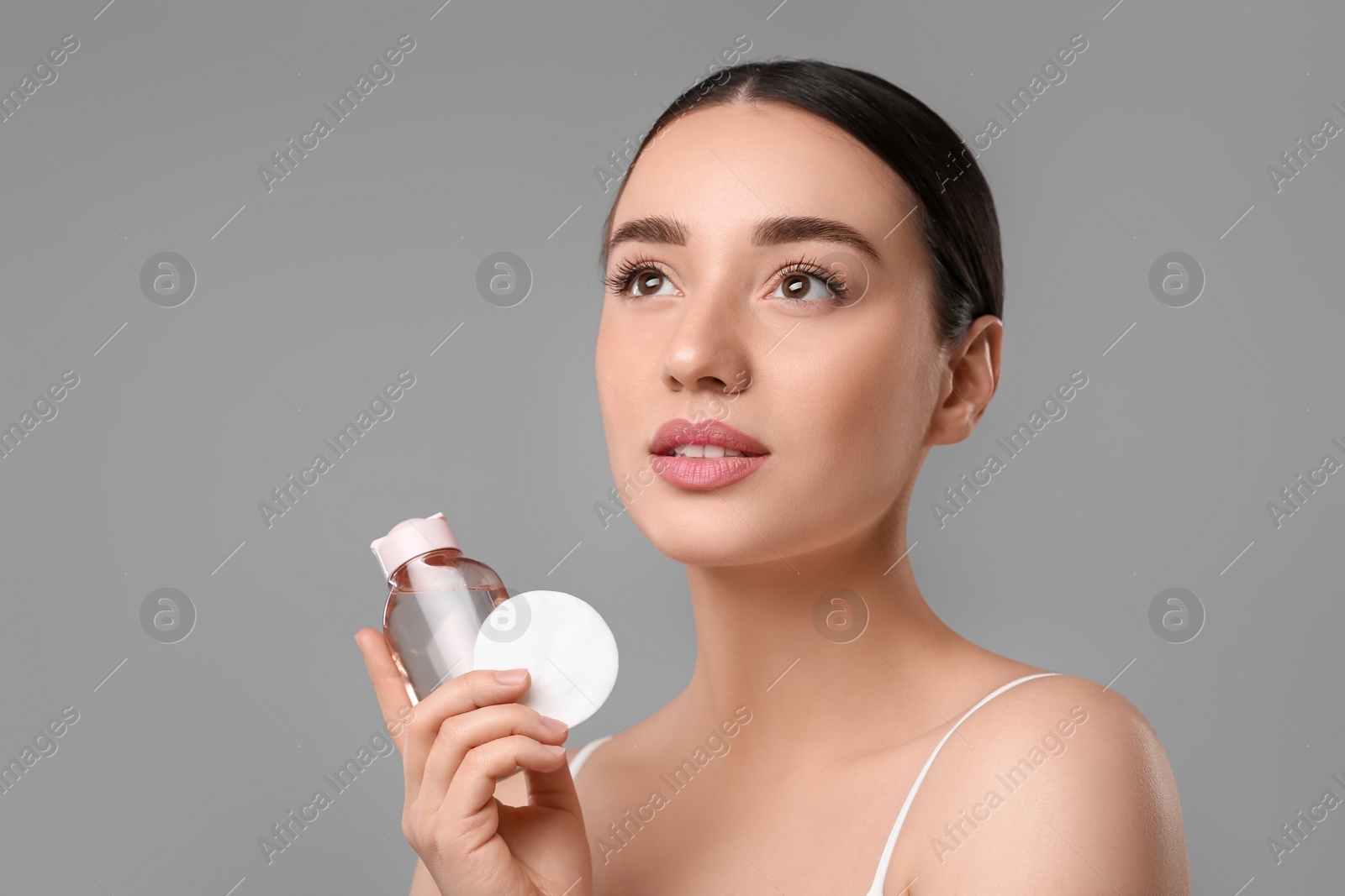 Photo of Beautiful woman with makeup remover and cotton pad on gray background, space for text