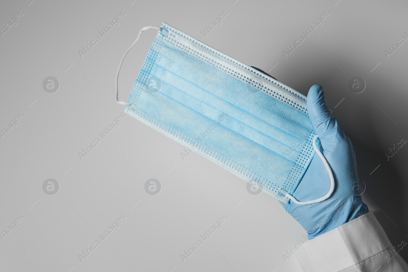 Photo of Doctor in latex gloves holding disposable face mask on light background, closeup with space for text. Protective measures during coronavirus quarantine