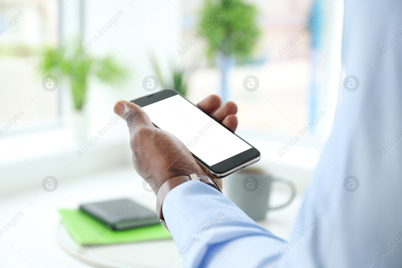 Photo of African-American man holding mobile phone with blank screen in hand indoors