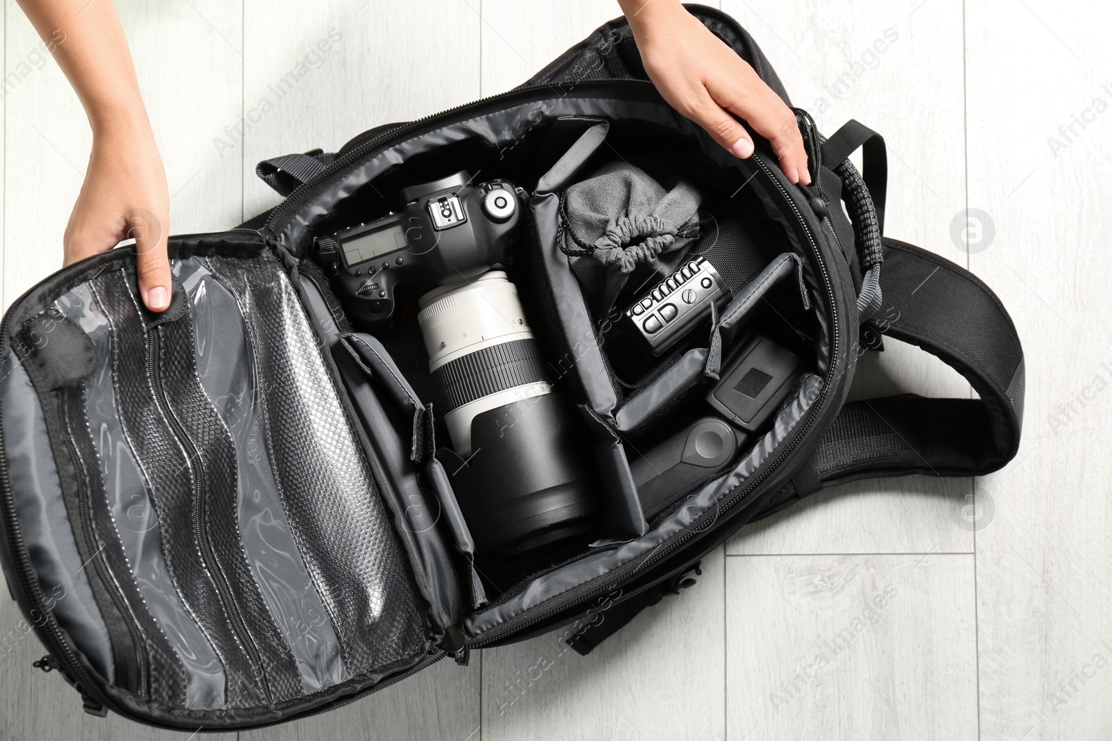 Photo of Woman putting professional photographer's equipment into backpack on floor, top view