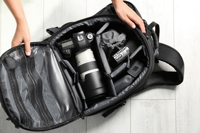 Woman putting professional photographer's equipment into backpack on floor, top view