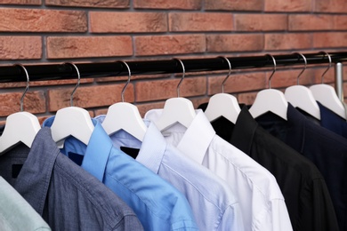 Wardrobe rack with stylish clothes near brick wall, closeup