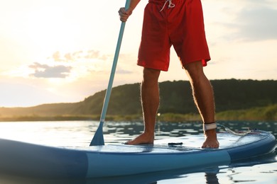 Photo of Man paddle boarding on SUP board in river at sunset, closeup