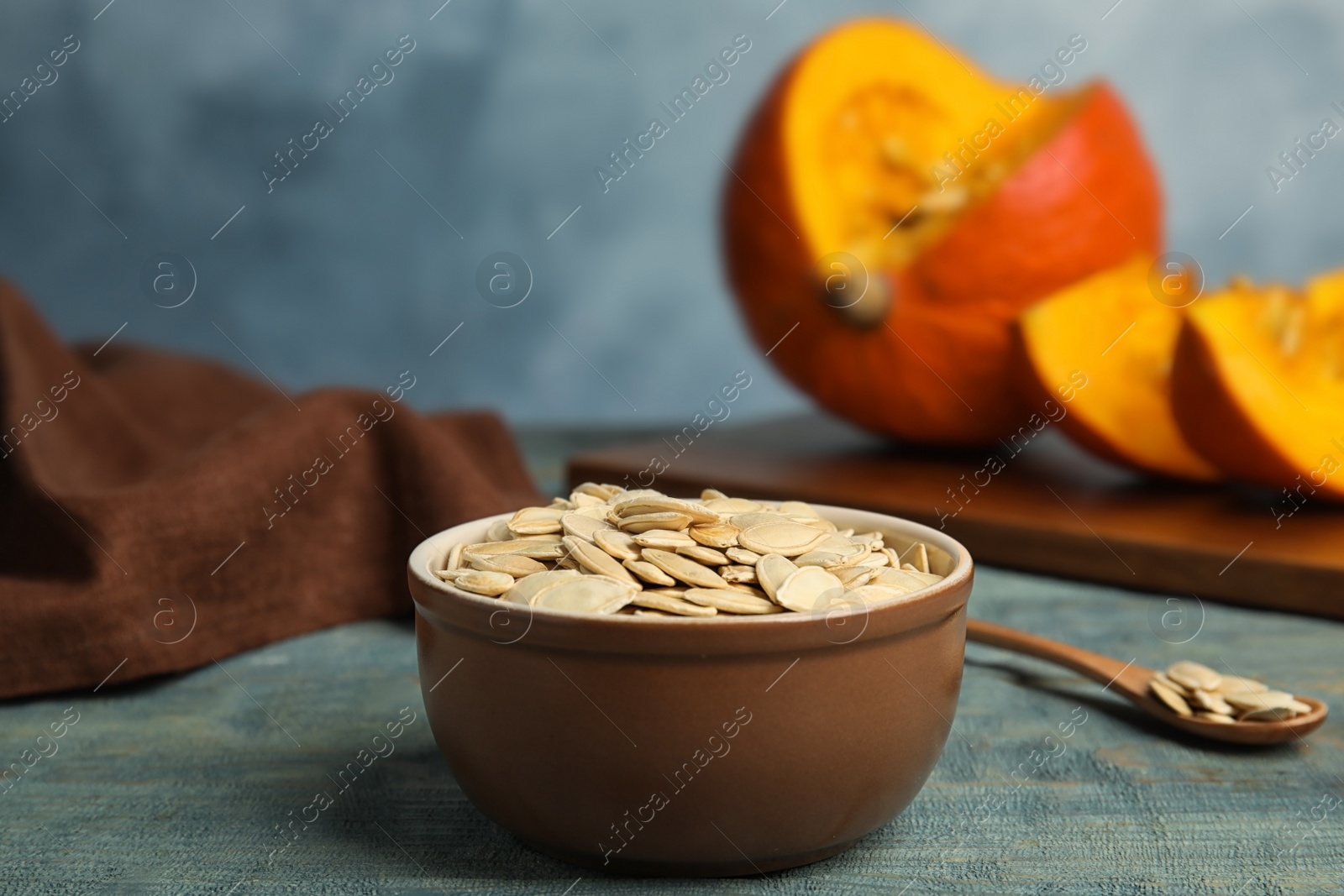 Photo of Bowl of raw pumpkin seeds on blue wooden table