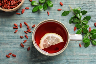 Photo of Healthy goji tea with lemon in cup on blue wooden table, flat lay