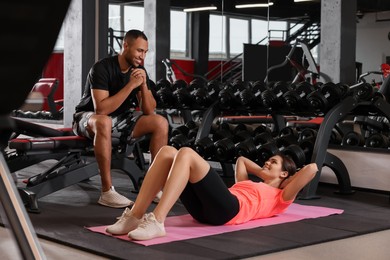 Photo of Trainer looking at woman while she doing exercise in modern gym