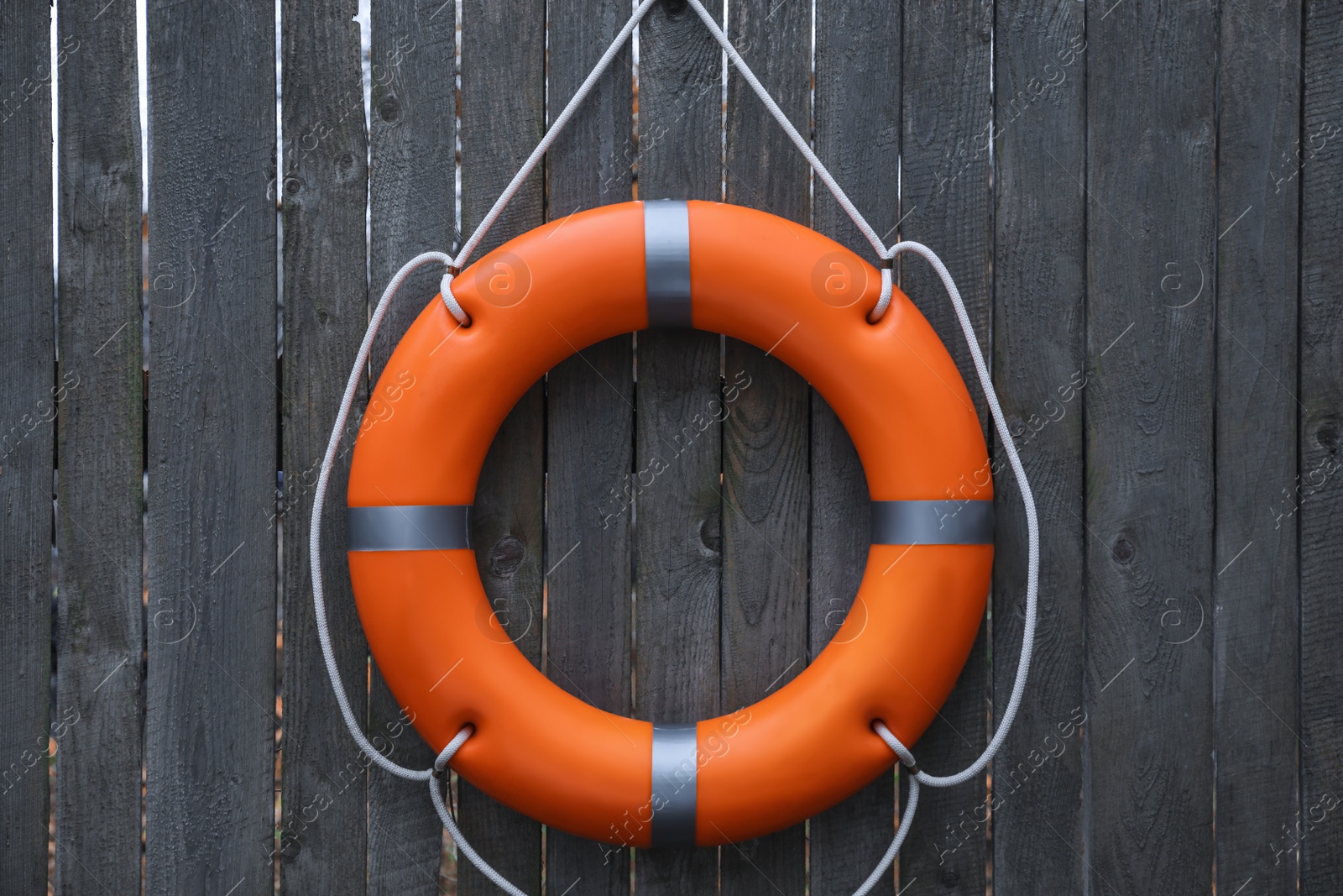 Photo of Orange lifebuoy hanging on grey wooden fence. Rescue equipment