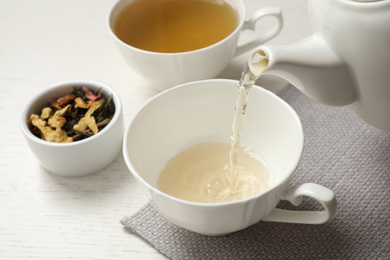 Photo of Pouring green tea into cup on white wooden table