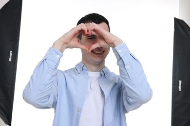 Photo of Man looking through folded in shape of heart hands on white background