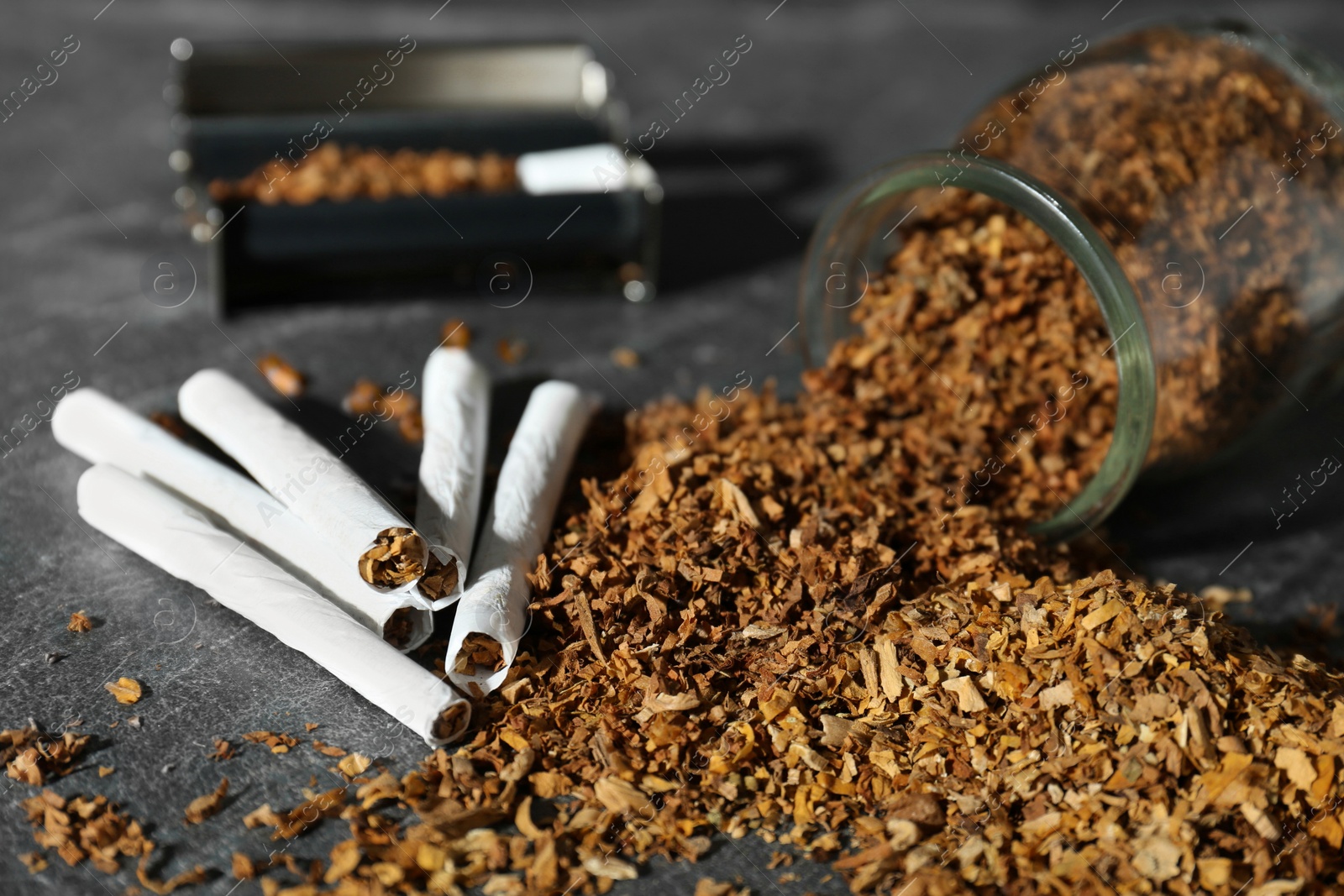 Photo of Tobacco, hand rolled cigarettes and roller on dark grey table, closeup