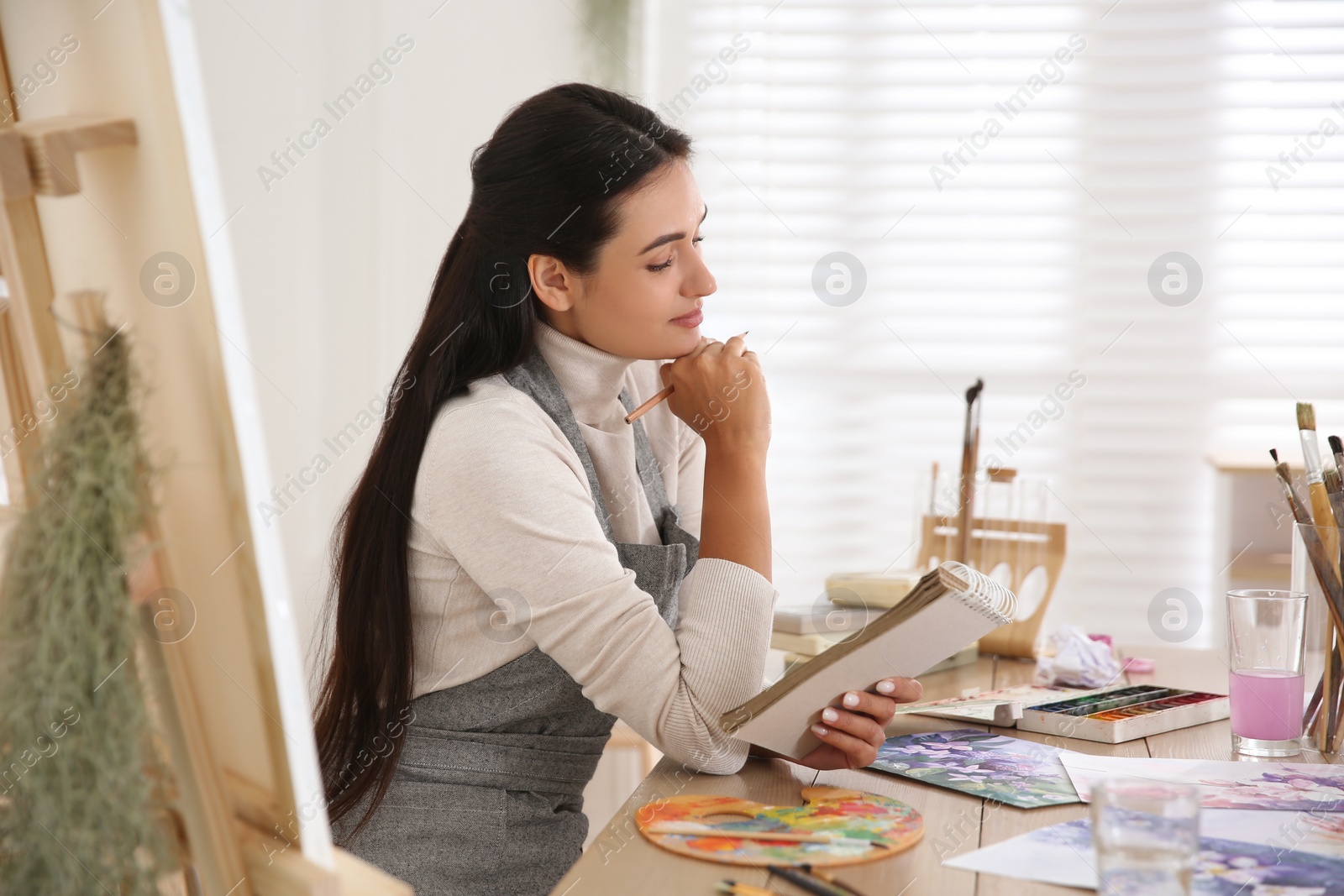 Photo of Young woman drawing in notebook at table indoors