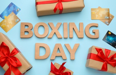 Photo of Text Boxing Day of wooden letters, credit cards and gifts on light blue background, flat lay. Sale concept