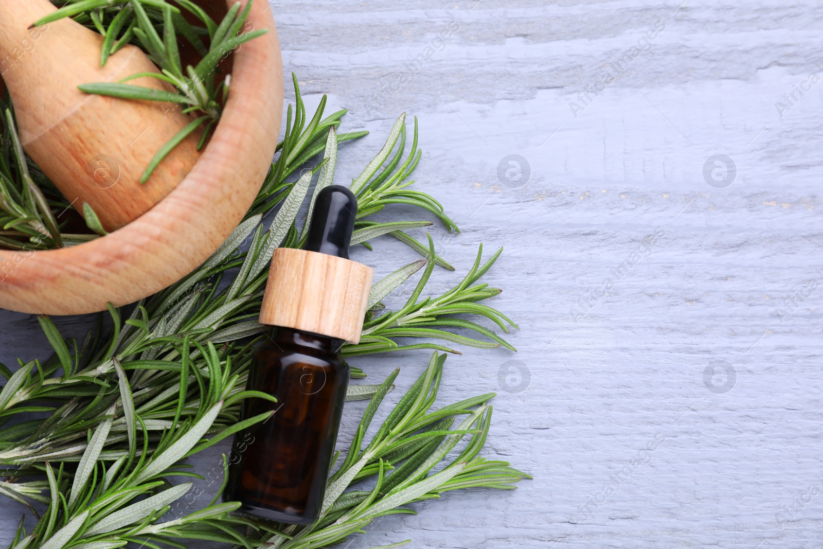 Photo of Bottle of rosemary essential oil on wooden table, flat lay. Space for text