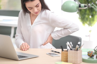 Young woman suffering from back pain in office