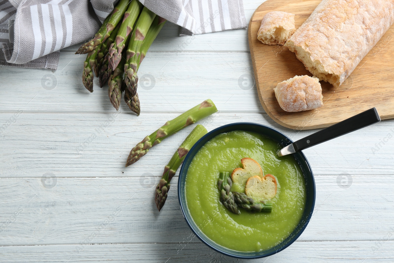 Photo of Delicious asparagus soup in bowl on white wooden table, flat lay