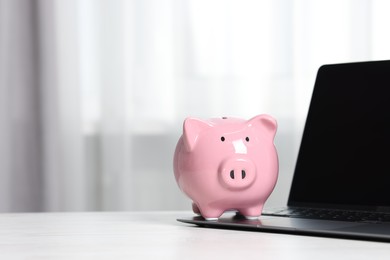 Photo of Piggy bank and laptop on white table indoors. Space for text