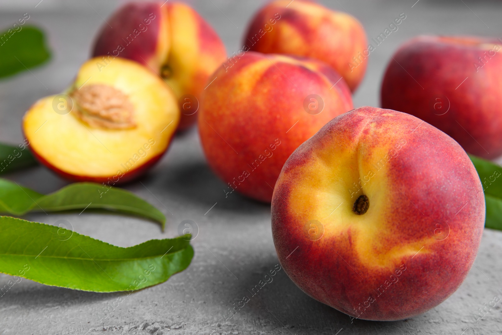 Photo of Fresh peaches and leaves on grey table