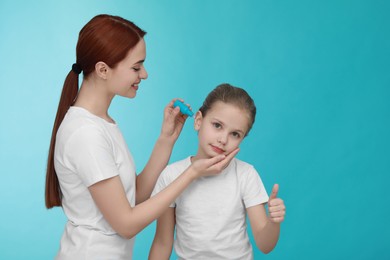 Mother dripping medication into daughter's ear on light blue background. Space for text