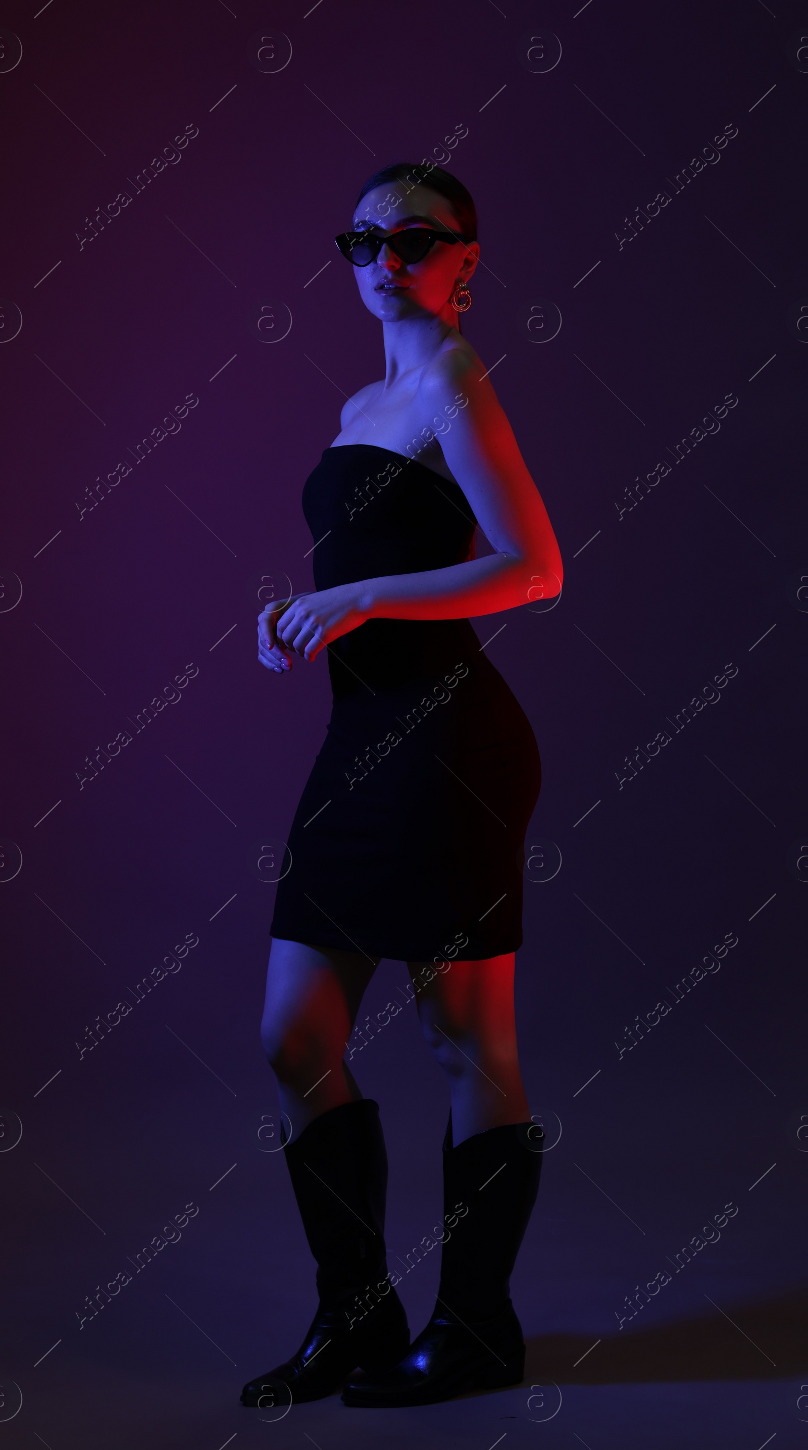 Photo of Full length portrait of beautiful young woman in sunglasses on color background with neon lights