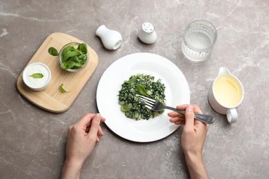 Photo of Young woman eating tasty spinach at grey marble table, flat lay. Healthy food