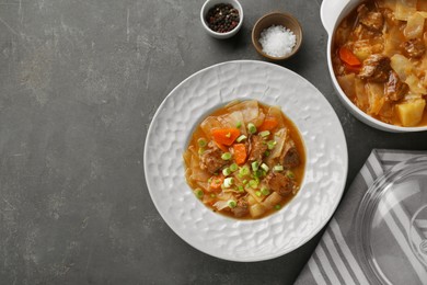 Photo of Tasty cabbage soup with meat, green onion and carrot served on grey table, flat lay. Space for text