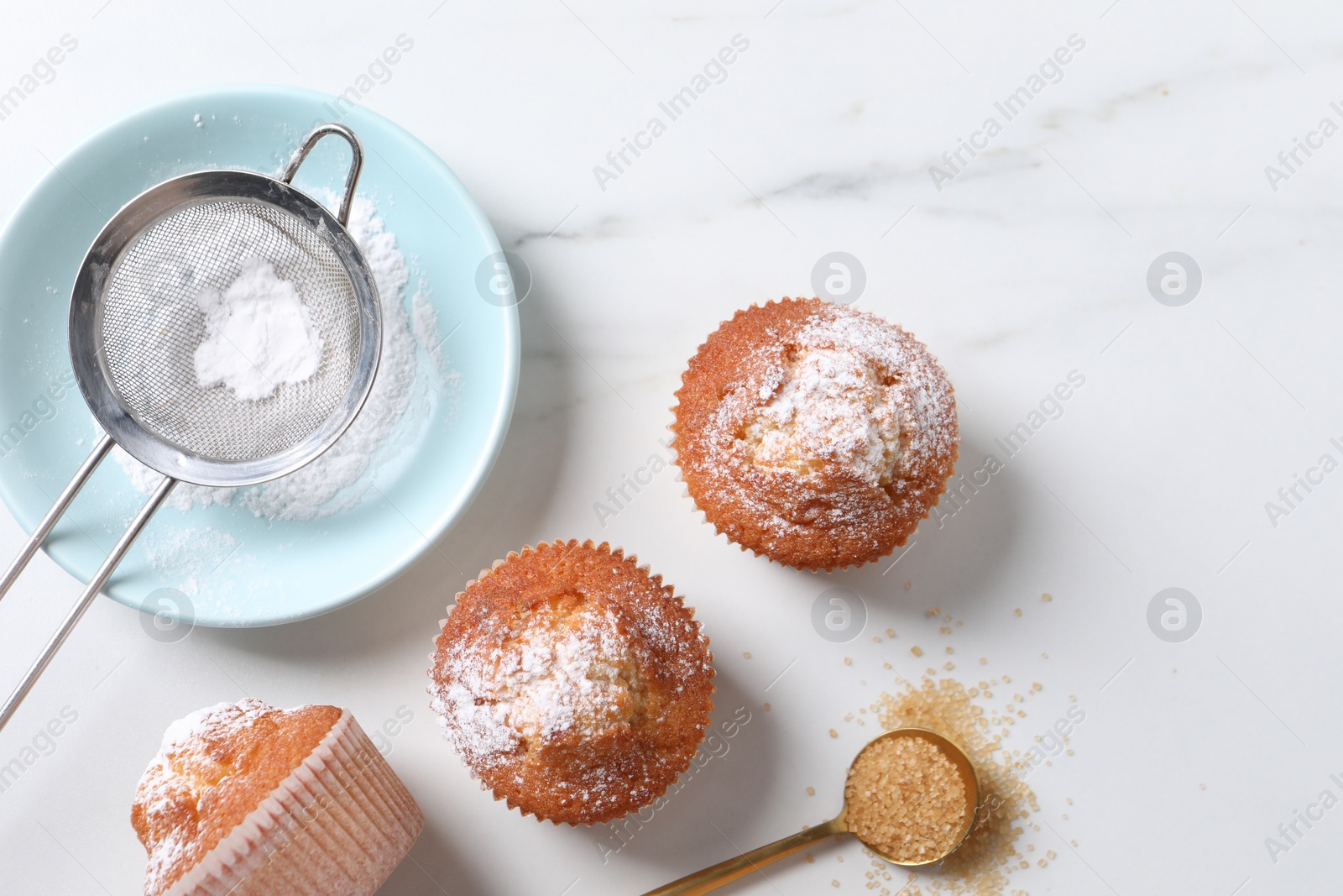 Photo of Delicious sweet muffins, plate and sieve on white marble table, flat lay, Space for text