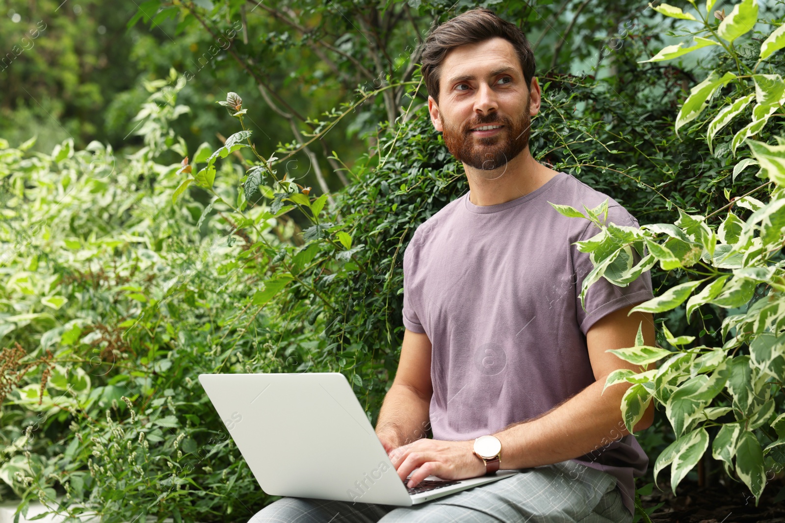 Photo of Handsome man with laptop in green garden