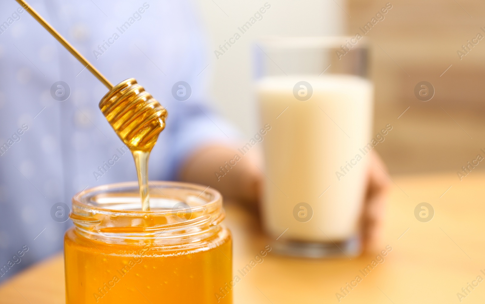Photo of Woman holding honey dipper over jar at wooden table, closeup. Space for text