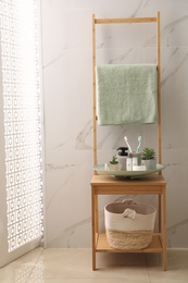 Photo of Holder with toothbrushes, different toiletries and plants on wooden rack in bathroom